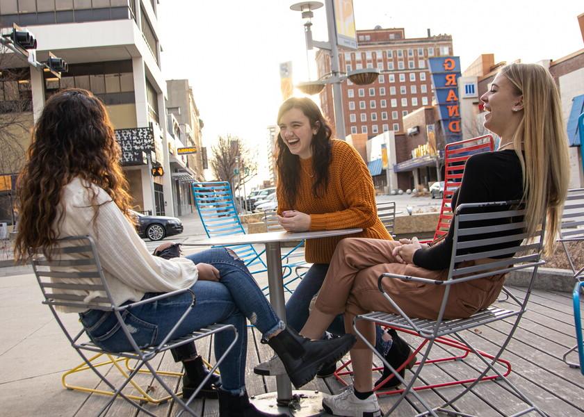 Four female NWU students sit at a table on the sidewalk of downtown Lincoln.